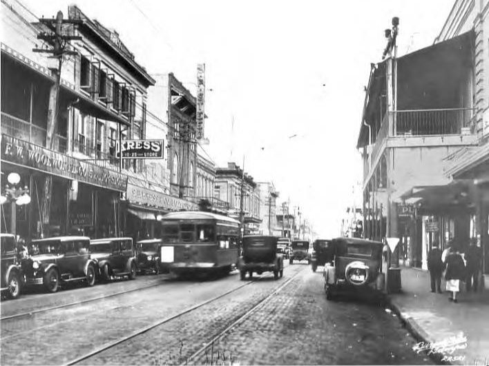 Ybor City's Seventh Ave; view west with automobiles, trolleys, and commercial buildings in 1927.