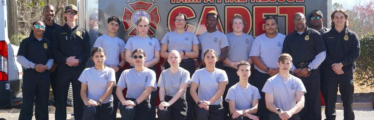 Group of Tampa Fire Rescue cadets and leaders posing in front of a cadet program trailer.
