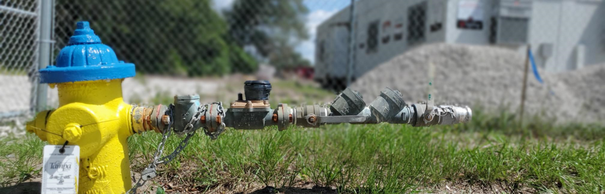 Portable water meter attached to a yellow fire hydrant near a construction site.