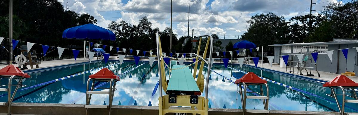 Outdoor swimming pool at Del Rio with diving board, lifeguard chairs, and blue umbrellas.