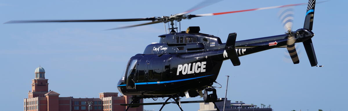 Police helicopter hovering over a runway with city buildings in the background.