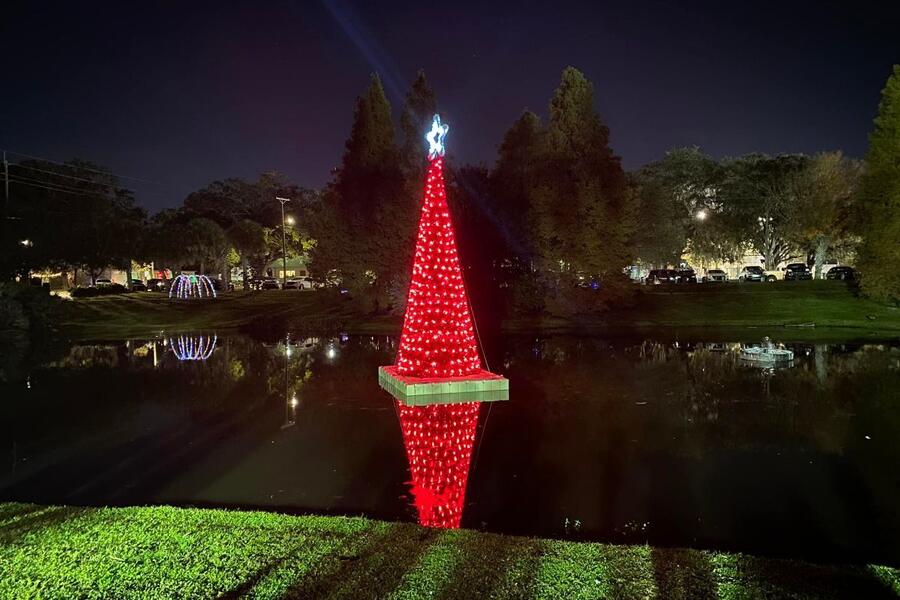 Red Christmas tree with lights reflected in a pond at night.