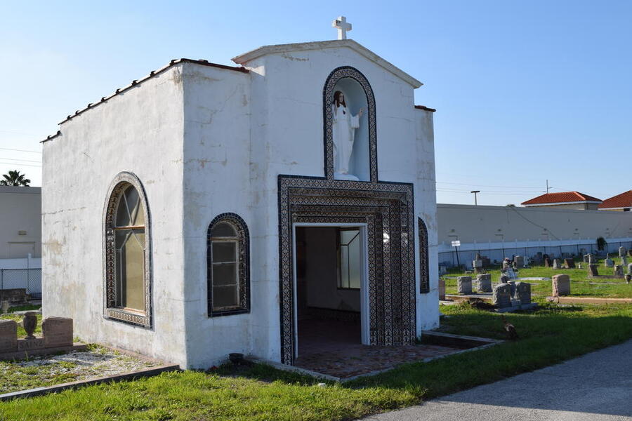 White mausoleum with arched windows in a cemetery, under a clear blue sky.