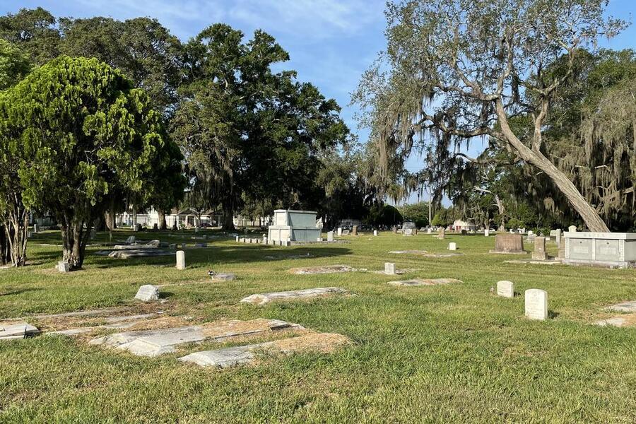 Peaceful cemetery with gravestones, trees, and a clear blue sky.