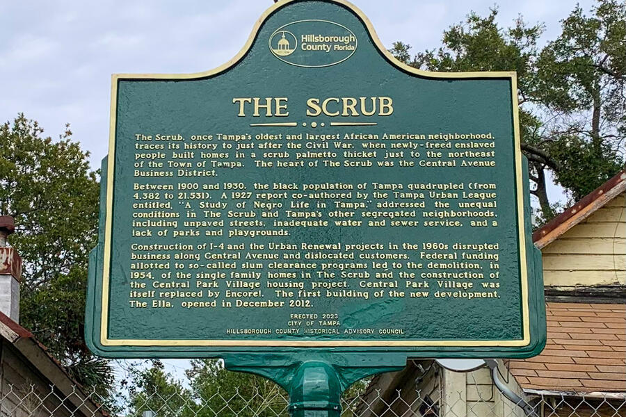 Historic marker titled "The Scrub" detailing local history, surrounded by trees.