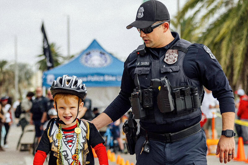 Child on a bike with a police officer at a bicycle safety event outdoors.