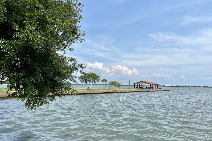 Coastal area with calm waters, trees, and a small structure at Palmetto Beach under a blue sky.