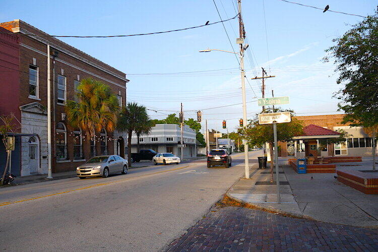 Street view in West Tampa with brick buildings, palm trees, and parked cars.