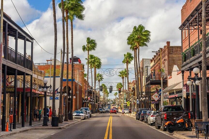 Street view of Ybor City, lined with historic buildings and palm trees under a cloudy sky.