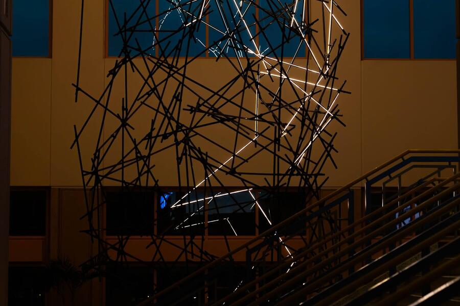 Large abstract metal sculpture resembling lightning in a modern indoor setting near stairs.