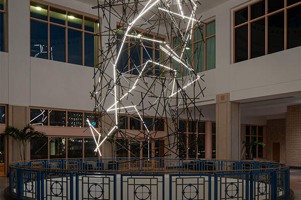 Tall indoor light sculpture resembling a zigzag lightning bolt on metal scaffolding.