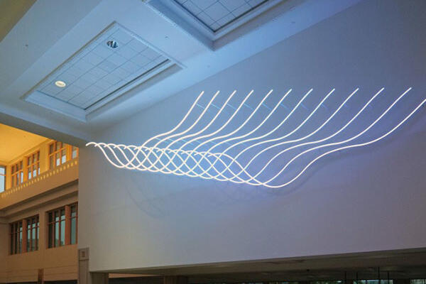 Curved light installation on a wall, resembling recurring wave patterns in a modern interior.