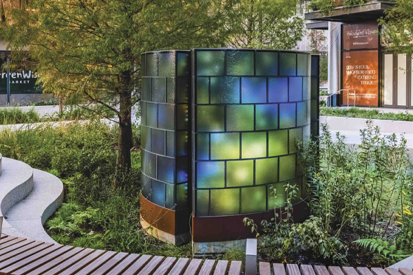 Curved structure with three colored glass arcs in a landscaped urban park.