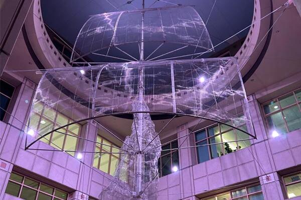 Large translucent sculpture resembling rising smoke, suspended in an atrium with purple lighting.