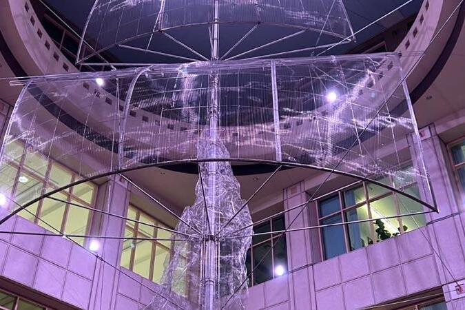 Translucent smoke-like sculpture rising indoors at night, lit by purple lights.