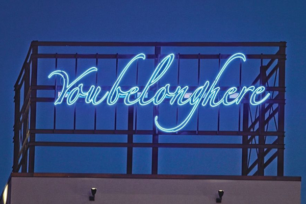 Neon sign reading "You belong here" glowing against a dark blue sky.