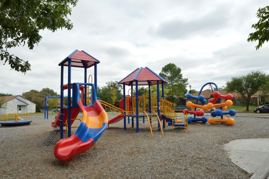 Colorful playground with slides, climbing structures, and swings on a gravel surface outdoors.