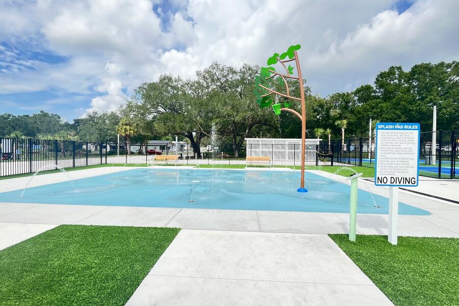 Shallow splash pad with a palm tree water feature at Fair Oaks park, surrounded by greenery.