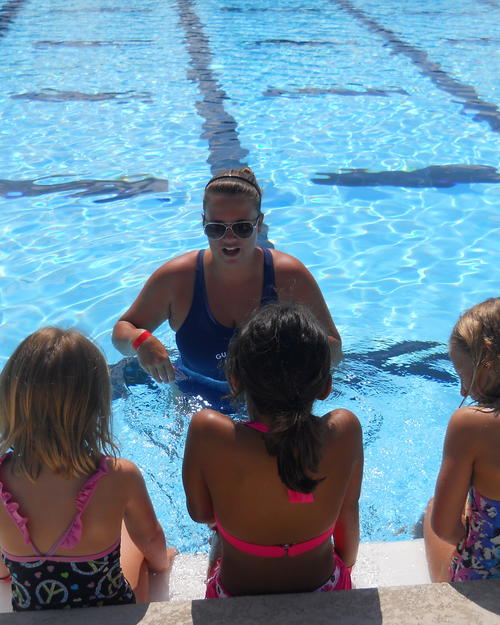 Instructor in water with students sitting on pool wall