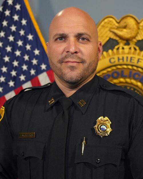 Police captain in uniform in front of a flag and badge display.