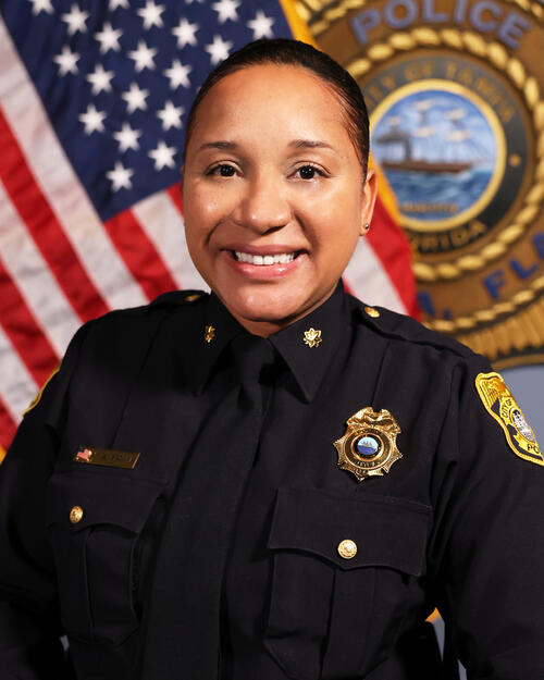 Major Kim Fruit in a police uniform, smiling, with a U.S. flag and police emblem backdrop