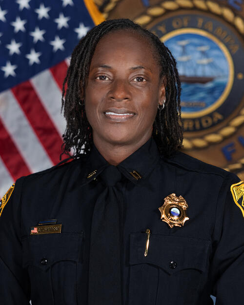 Captain Peterson in formal uniform smiling, badge visible, with American and Florida flags in background.