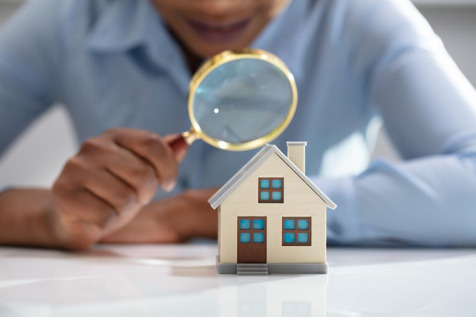 Person inspecting small house model with magnifying glass.