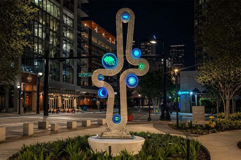 Modern sculpture with illuminated circles, symbolizing unity, in an urban plaza at night.