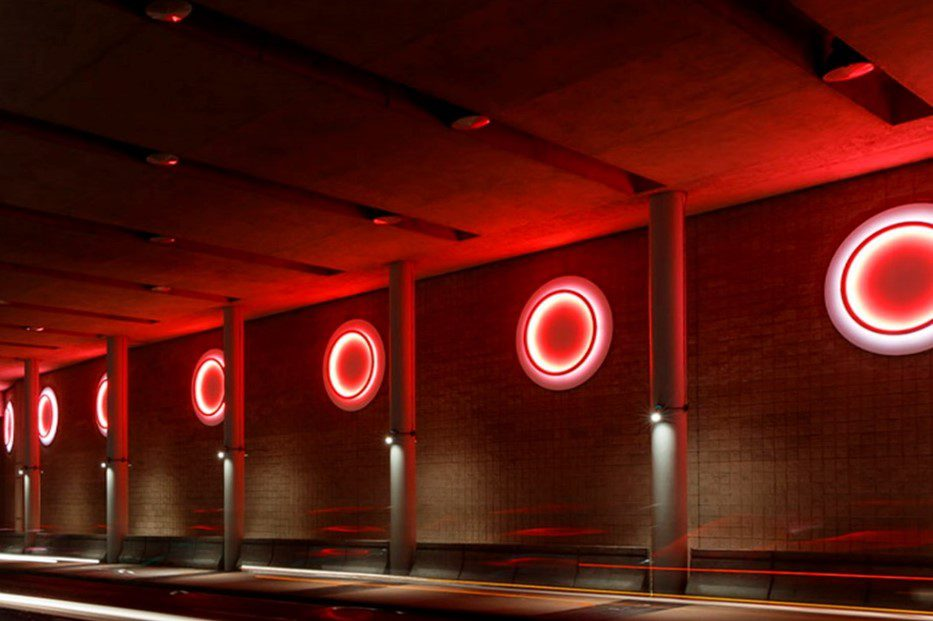 Red neon circles glowing on a brick wall, suggesting unity and repetition in a modern hallway.
