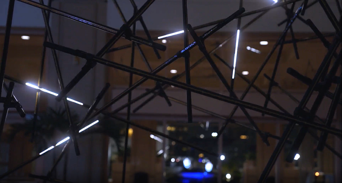 Abstract sculpture with illuminated rods resembling lightning, displayed indoors.