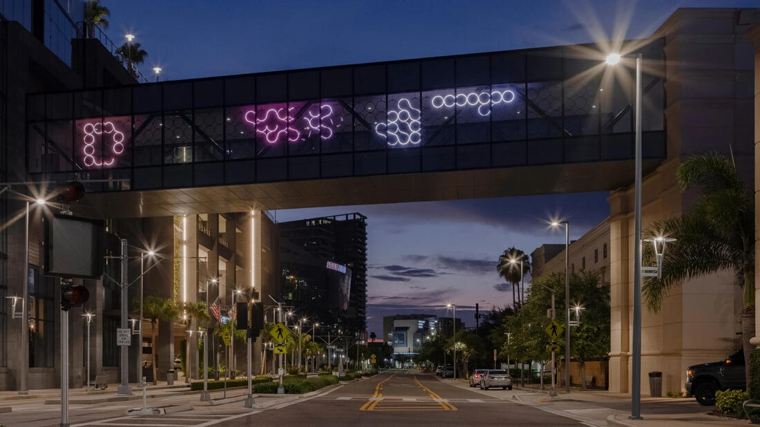 Street at dusk with a skybridge displaying colorful abstract neon lights.