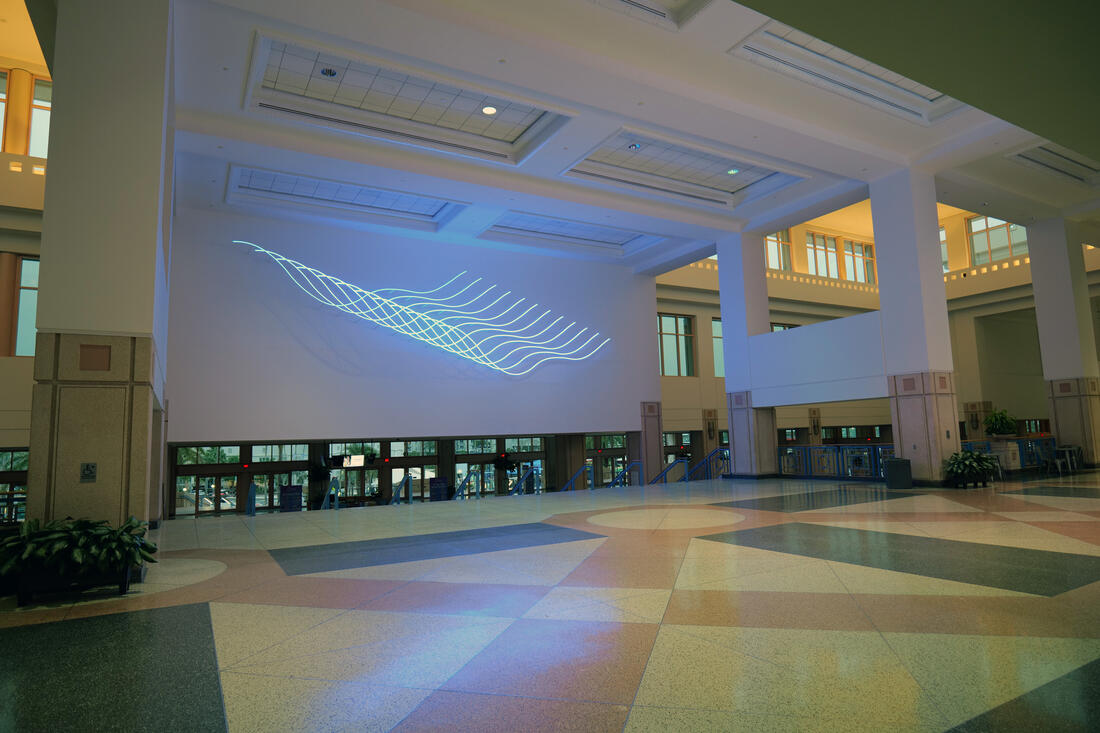 Large indoor atrium with geometric light art by Luftwerk projected on the wall.