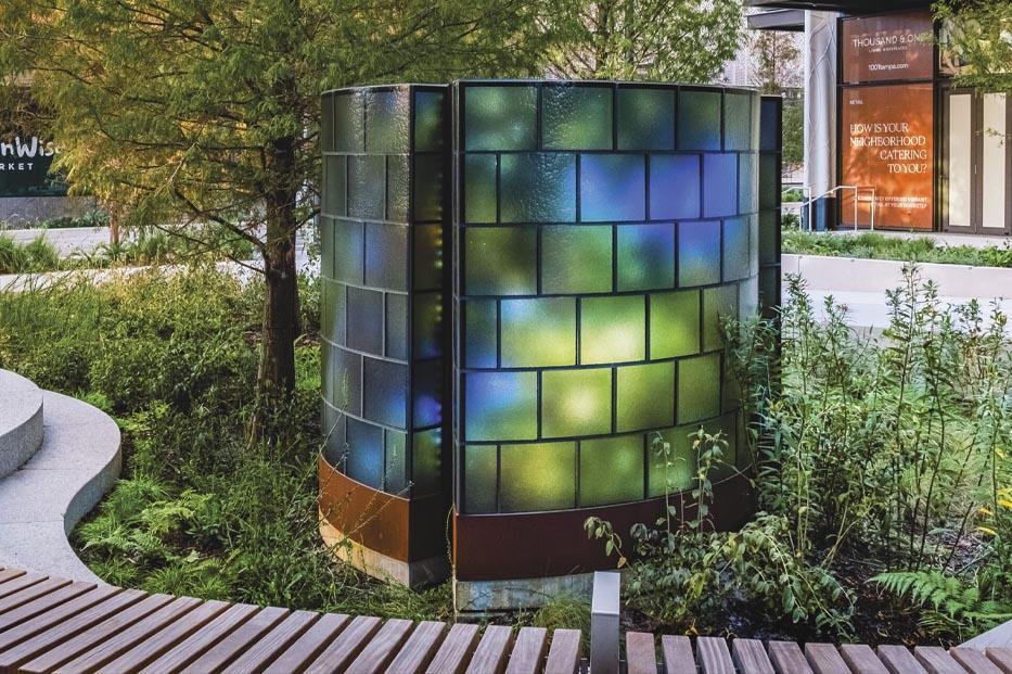 Curved glass structure with colorful panels, resembling three arcs, set in a landscaped garden.