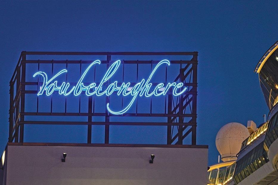 Neon sign reading "You belong here" glowing against a deep blue evening sky.