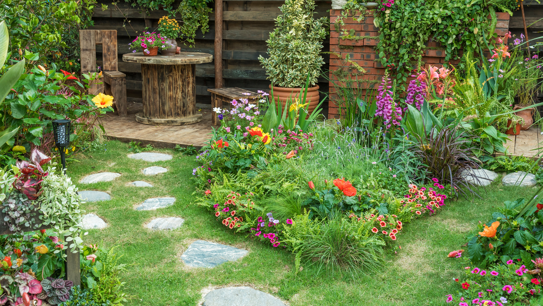 Lush garden with colorful flowers, stone path, and a rustic wooden table in the background.
