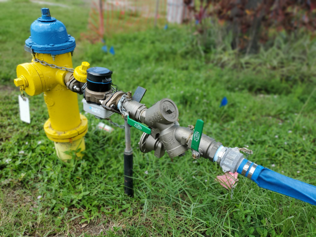 Portable hydrant water meter attached to yellow fire hydrant on green grass background.