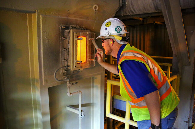Worker inspecting waste-to-energy furnace through small window.