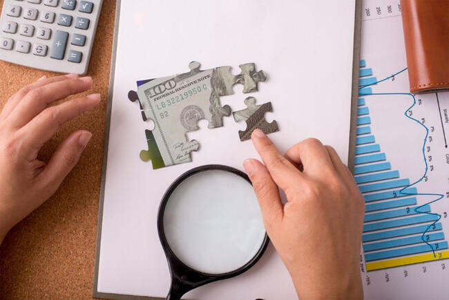 Hands assembling puzzle pieces over a paper, graph, and magnifying glass.