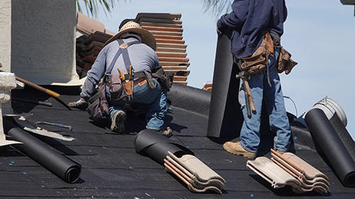 Workers installing roofing materials on a sloped rooftop.