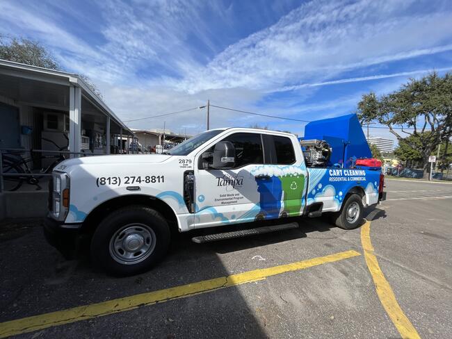 White truck parked in a lot, blue and green markings, clear sky above.