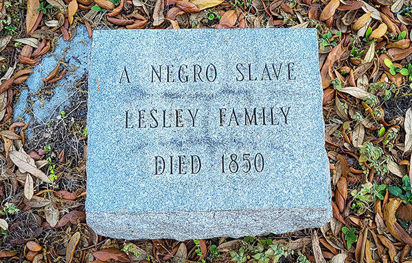 Gravestone reading &quot;A Negro Slave, Lesley Family, Died 1850&quot; surrounded by leaves.