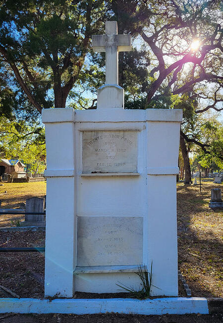 White tombstone of Vicente M. Ybor in a sunlit cemetery with a cross on top.