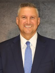 Smiling man in a suit and tie against a gray background.