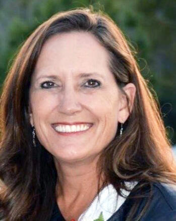 Heather Erickson smiling outdoors, with long brown hair and a white top.