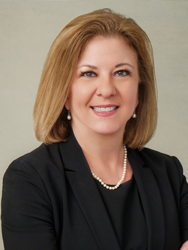 Professional woman smiling in a suit, wearing pearl earrings and necklace.