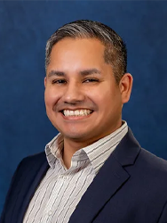 Smiling man in a suit against a blue background.