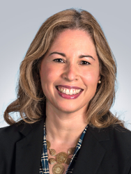 Smiling woman with wavy hair wearing a blazer and checkered top.