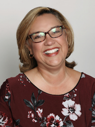 Smiling woman with glasses in a floral blouse, neutral background.