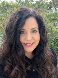 Smiling woman with long curly hair in a garden setting.