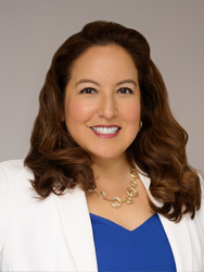 Smiling woman in a white blazer with curly hair and a blue top.